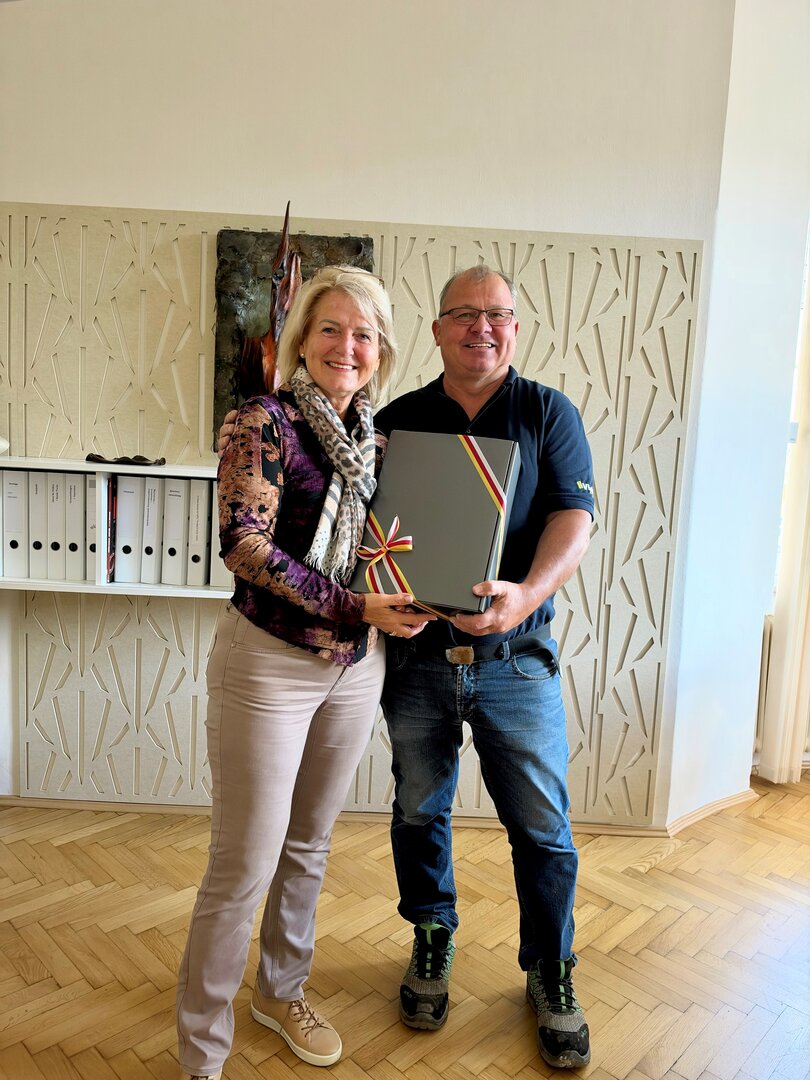 Frau und Herr überreichen Geschenkkorb vor Wanddekoration und Aktenordnern